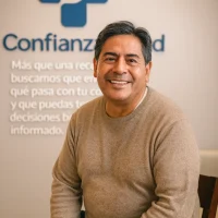 Paciente adulto sonriente en el consultorio de Confianza Salud con el logo al fondo, símbolo de confianza y decisiones informadas sobre la salud del corazón.